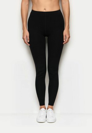 Leggings negros con un diseño ajustado, hechos de un tejido elástico. Presentan una cinturilla alta y una textura suave, combinados con zapatillas blancas.