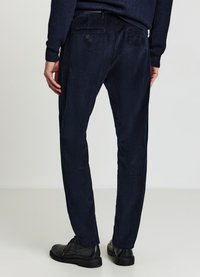 Marineblaue Cordhosen mit strukturierter Oberfläche, maßgeschneiderter Passform und zwei Gesäßtaschen. Kombiniert mit schwarzen Lederschuhen.