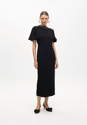 Black midi dress with short flared sleeves and beaded neckline detail. Worn with black slingback heels featuring bow accents.