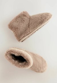 Vaatteiden jäljitelmällä valmistetut nilkkasaappaat pehmeässä beigen värissä, pyöristetyllä kärjellä, ylellisellä rakenteella ja paksulla pehmustetulla pohjalla. Avoin yläosa helpottaa pukemista.