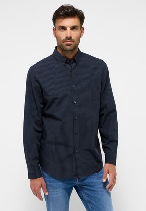 Camisa de manga larga a cuadros en azul oscuro con cuello abotonado, bolsillo en el pecho y botones en el frente, combinada con jeans azul claro.