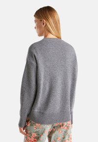 Pull en tricot gris à la coupe ample et à bord côtelé, avec un col rond et des manches longues, porté avec un pantalon à motifs floraux.