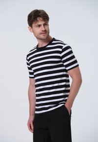 Sort og hvid stribet kortærmet t-shirt med rund hals, lavet af blødt stof, præsenteret mod en ensfarvet lys baggrund.