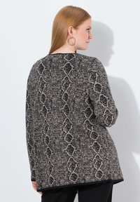 Sweter dzianinowy z czarnym i kremowym wzorem w węża, długimi rękawami, luźnym krojem i zaokrąglonym dołem, w połączeniu z okrągłymi kolczykami.