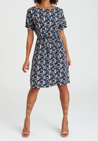 Abito floreale al ginocchio in blu navy, con maniche corte, vita elastica e motivi astratti multicolori. Indossato con tacchi nudi a strappo.