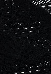 Svart stickad tröja med intrikata öppna mönster, strukturerade stygn och ribbade ärmmuddar som visar en variation av stickade designer.