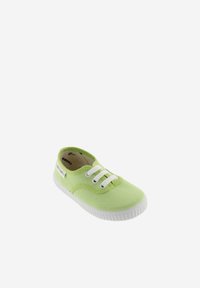 Zapato de lona verde claro con cordones blancos, punta redondeada y suela de goma texturizada. Etiqueta de marca visible en el lateral.