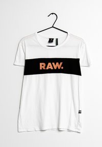 Biały t-shirt z krótkimi rękawami, z czarnym poziomym paskiem z napisem "RAW." w kolorze pomarańczowym. Wykonany z miękkiej bawełny.