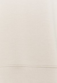 Tissu beige avec un détail de couture horizontale sur la partie inférieure, montrant la texture et les points de couture.