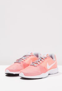 Baskets de sport en mesh rose avec des accents blancs, présentant une tige texturée, un bout arrondi et des lacets gris. Logo Nike de chaque côté.