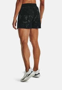 Svarta sportshorts med ett texturerat mönster, elastisk midja och en lös passform, kombinerat med vita sneakers med en svart logotyp.