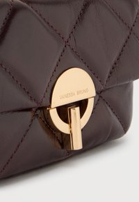 Μπορντό δερμάτινη τσάντα με καπιτονέ σχέδιο, διαθέτει στρογγυλό κούμπωμα σε χρυσαφένιο τόνο με χαραγμένο το "VANESSA BRUNO", αναδεικνύοντας την λεία υφή και τη λάμψη.