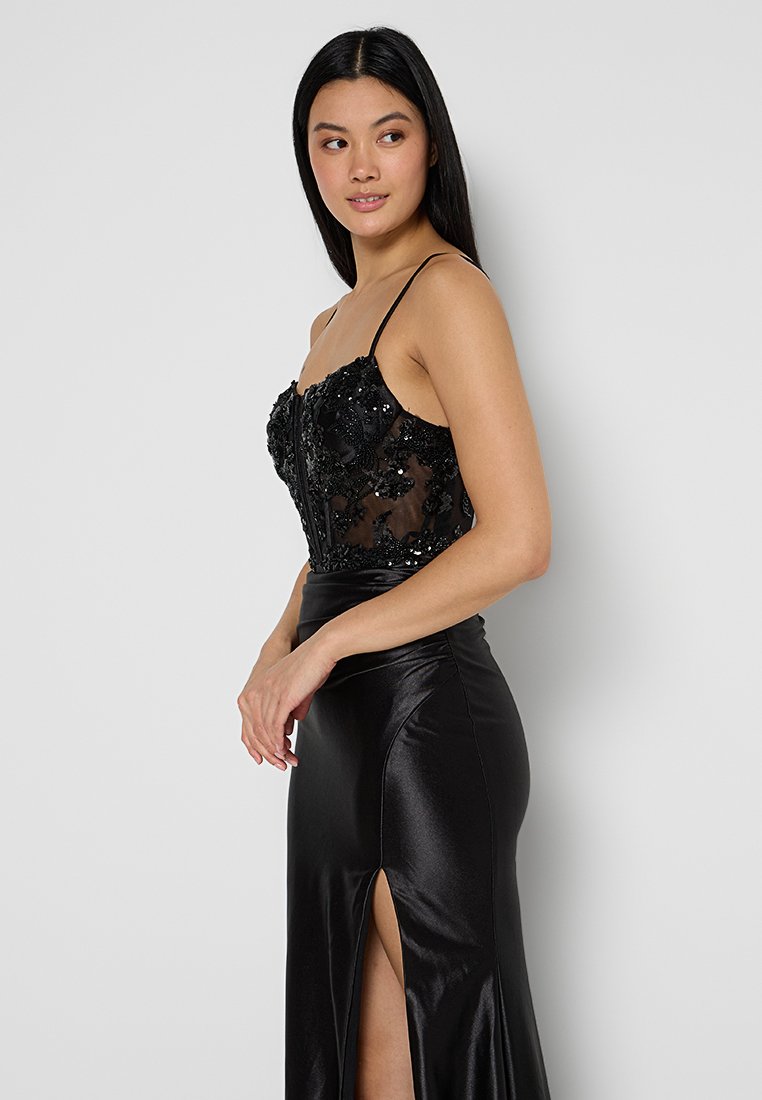 Abito da sera nero con un corpetto trasparente ricamato con perline, spalline sottili e una gonna in satin liscia con una spacco laterale.