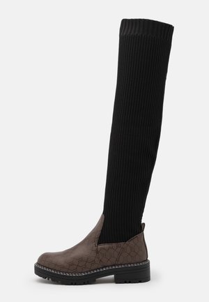 Botte montante en tissu côtelé noir avec tige en cuir texturé marron, dotée d'une semelle crantée noire et d'une languette au talon.