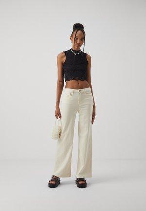 Svart blonde crop topp, brede kremfargede bukser, kraftige svarte sandaler og en liten perleveske med teksturert overflate.
