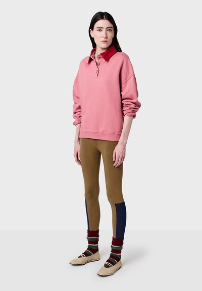 Pink pullover sweatshirt with a red collar and three buttons, paired with brown leggings featuring a navy blue accent, striped knee-high socks, and beige shoes.