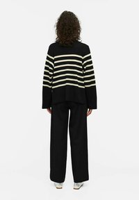 Maglione a righe nero e beige con maniche lunghe, abbinato a pantaloni neri a gamba larga e scarpe argentate lucide. Tessuto lavorato a maglia, vestibilità rilassata.