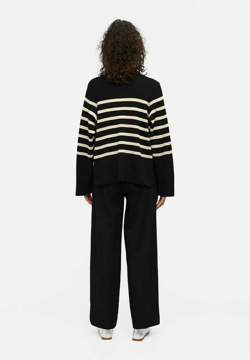 Pull rayé noir et beige à manches longues, associé à un pantalon large noir et des chaussures argentées brillantes. Texture tricotée à la machine, coupe décontractée.