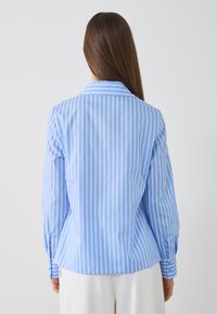 Light blue button-up shirt with white vertical stripes, long sleeves, and a classic collar. Smooth cotton fabric with a tailored fit.