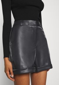 Czarne szorty z imitacji skóry o gładkiej fakturze i podwiniętych brzegach. Posiadają boczne kieszenie i dopasowany pas, który doskonale komponuje się z prążkowanym topem.