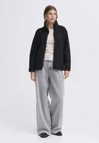 Must musta jope kõrge kraega, kombineeritud heledate hallide laiade püksidega. Kanga näeb välja pehme koos tekstuurse, pehme viimistlusega.