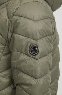 Olivengrønt, polstret jakke med quiltet design, der har et logo patch på ærmet. Stoffet har en glat, blank overflade.