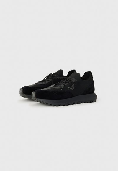 Black athletic shoes made of suede and mesh, featuring a textured sole, laces, and a small logo accent on the side.