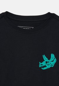 Schwarzes Baumwoll-T-Shirt mit Rundhalsausschnitt, das auf der linken Brust ein türkisfarbenes Dinosaurierschädel-Design aufweist. Weicher Stoff, lässiges Design.