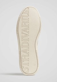 Semelle de chaussure de sport de couleur crème avec une surface texturée ; comporte le nom de la marque "STRADIVARIUS" en relief et un indicateur de taille marqué 37.