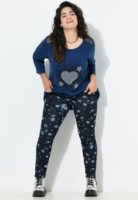 Marineblauwe lange mouwen shirt met een hart- en sterontwerp in rhinestones, gecombineerd met marineblauwe skinny jeans met een sterpatroon, en zilveren laarzen.