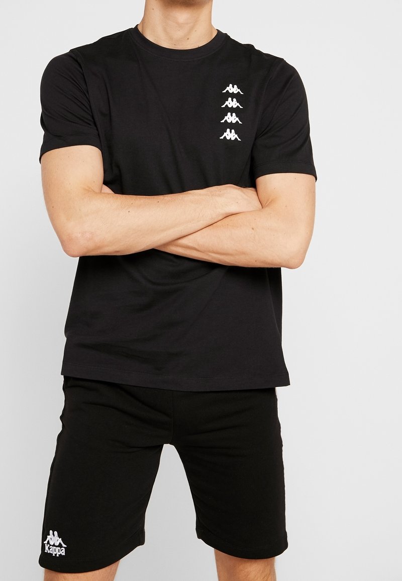 Černé triko Kappa s kulatým výstřihem, krátkými rukávy a bílými prvky loga. Spárováno s černými šortkami s bílým logem. Hladká tkanina.