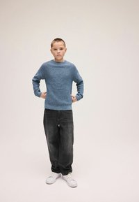 Niebieski sweter dzianinowy o fakturze, z okrągłym dekoltem, zestawiony z luźnymi, ciemnoszarymi dżinsami i białymi trampkami.