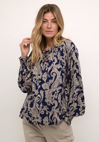 Tummansininen yllä, jossa on beige paisley-kuvio, rypistetty pääntie, jossa on pieni aukko, ja pitkät hihat, joissa on elastiset hihansuut.