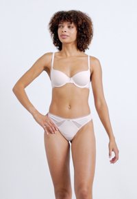 Soutien-gorge contour rose clair avec armatures et bretelles ajustables, associé à des culottes en dentelle à panneaux transparents assorties, présentées sur un mannequin.