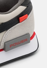 Sneaker z cholewką z zamszu w jasnoszarym kolorze, czarnymi akcentami, czerwoną metką oraz szarym piętą z napisem "POWER". Gruba biała i czarna podeszwa.