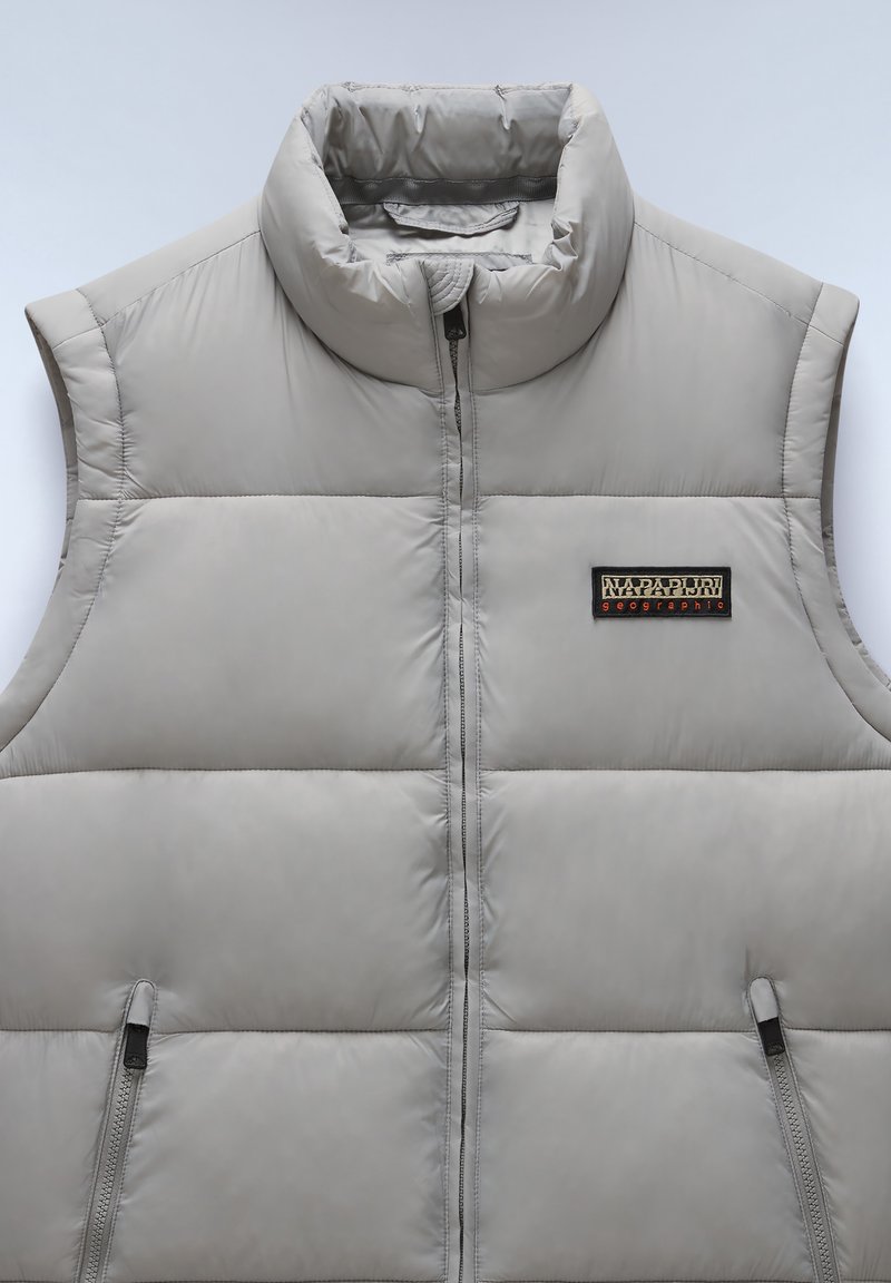 Smanicato imbottito grigio con colletto alto, dotato di due tasche con zip e una toppa con logo sul petto. Materiale liscio, leggero con design trapuntato.