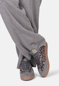 Sneaker con stampa leopardata, pannelli in suede grigio e tessuto, lacci blu navy, suole in gomma e design comodo, abbinate a pantaloni larghi grigi.