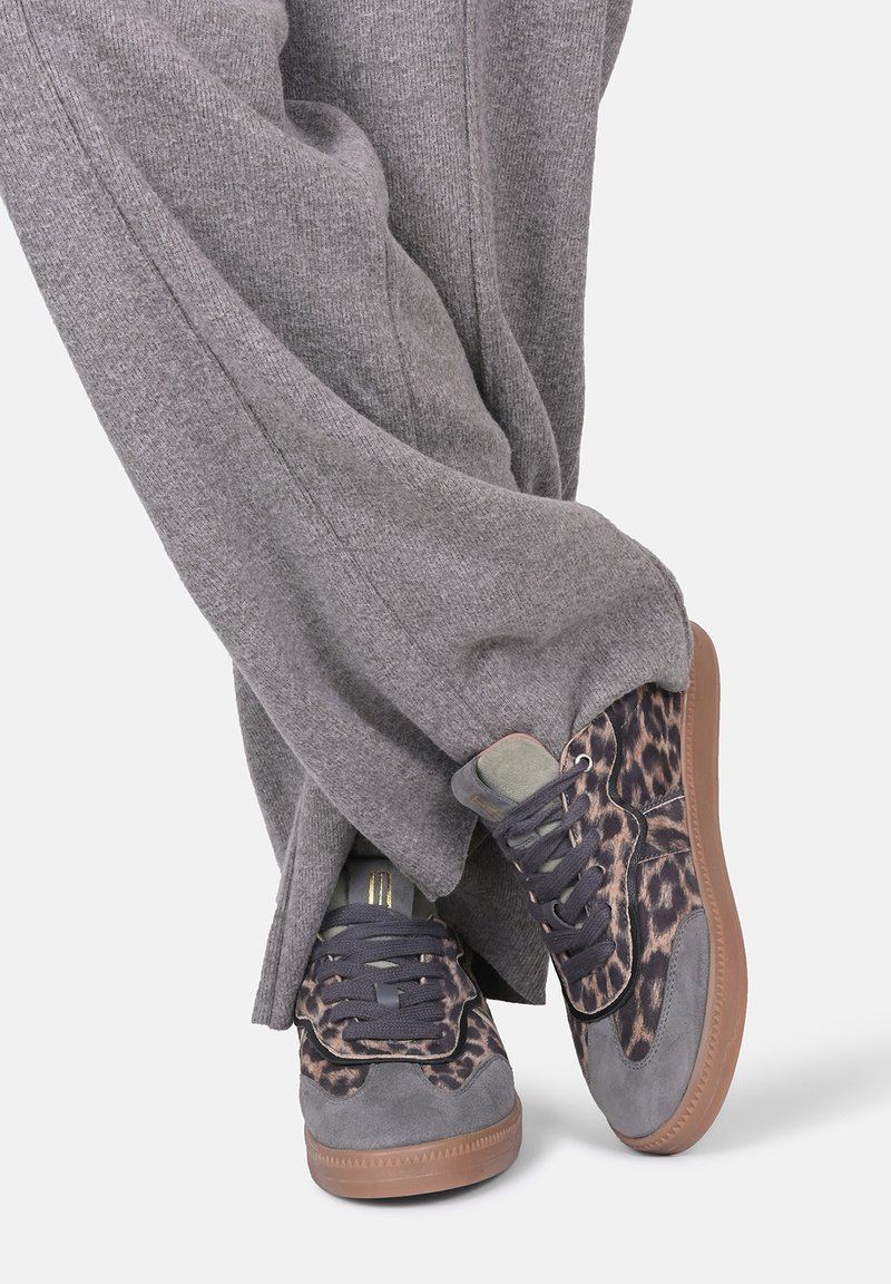 Sneaker con stampa leopardata, pannelli in suede grigio e tessuto, lacci blu navy, suole in gomma e design comodo, abbinate a pantaloni larghi grigi.