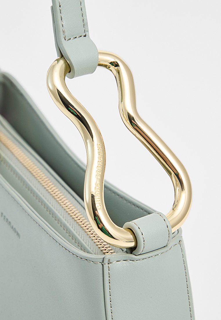 Hellgrüne Lederhandtasche mit glatter Textur, ausgestattet mit einem wellenförmigen goldenen Metallgriff und einem Reißverschluss, der sichtbare Nähte aufweist.