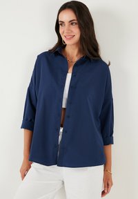 Camicia oversize blu navy in un tessuto morbido, con colletto, maniche a cuffia e una vestibilità rilassata.