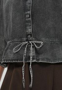 Γκρι denim τοπ με μαζεμένη μέση, με κορδόνι για δέσιμο, κούμπωμα με κουμπιά και λεπτές αποχρωματισμένες λεπτομέρειες.