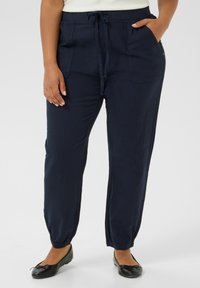 Pantalones tapered de color azul marino, hechos de una tela ligera, con cintura elástica y cordón ajustable, dos bolsillos laterales y puños elásticos.