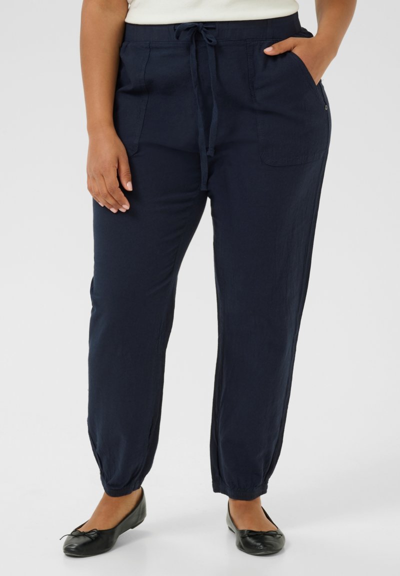 Pantalones tapered de color azul marino, hechos de una tela ligera, con cintura elástica y cordón ajustable, dos bolsillos laterales y puños elásticos.
