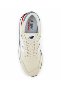 Zapatillas color tostado con detalles en blanco, parte superior de malla y suela negra. Cuenta con un cuello acolchado y un sistema de cordones clásico. Logo en la lengüeta.