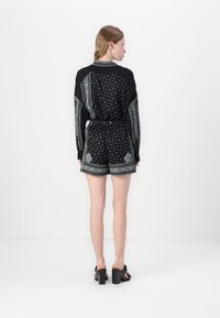 Svart romper med lange ermer, mønstrede accenter og shorts. Har intrikate grønne og hvite design langs ermene og kanten.