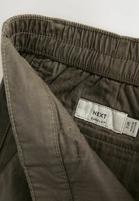 Grøn, letvægtig stof med en glat tekstur, der har en samlet talje og et mærke, der står "NEXT BARREL FIT 34R."
