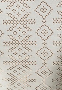 Beige Stoff mit einer strukturierten Oberfläche, der ein Quadratmuster aus kleinen Ausschnitten und Punkten aufweist, was ein rhythmisches Design schafft.