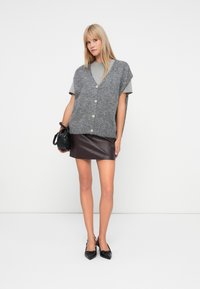 Sivé vlnené sako s véčkovým výstrihom a zapínaním na gombíky, vrstvené nad sivým tričkom. V kombinácii s vínovo červenou koženou mini sukňou a čiernymi lodičkami.