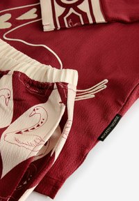 Roter Stoff kontrastiert mit cremefarbenen Shorts mit Schwanmuster. Enthält ein Etikett mit "ROCKETT & GEORGE". Strukturierter, lockerer Schnitt.