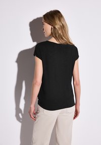 Top nero a maniche corte realizzato in un materiale leggero, con scollatura rotonda e vestibilità rilassata. Abbinato a pantaloni di colore chiaro.